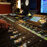 Audio engineer adjusting console faders during a mix at Somni Studios.